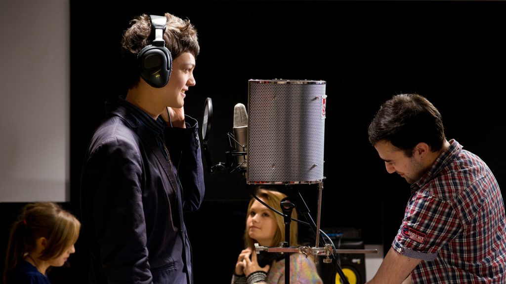 Student uses the recording studio in Creative Arts facilities. They are wearing headphones and talking into a microphone.