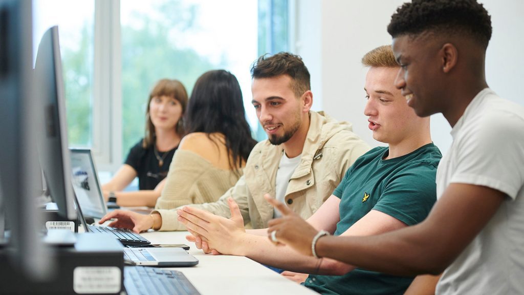 Students in computer lab looking at computers and talking to eachother