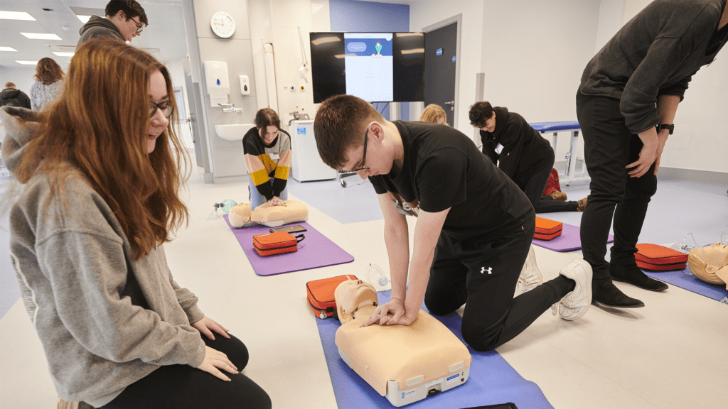 A student carries out chest compressions on a simulation patient while another student watches.