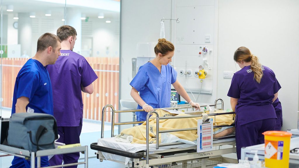 A group of health students in a simulation theatre treating a mannequin