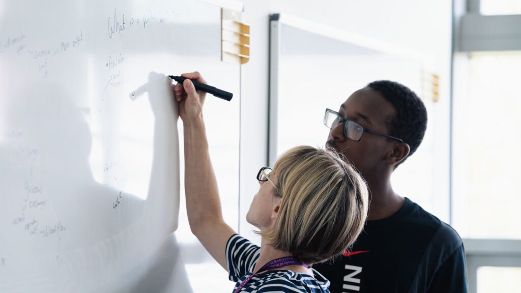 Tutor assisting student with writing on the whiteboard.