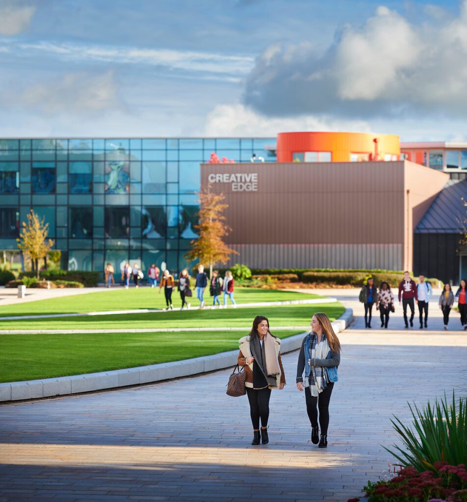 Two students walking across campus with the Creative Edge building in the background