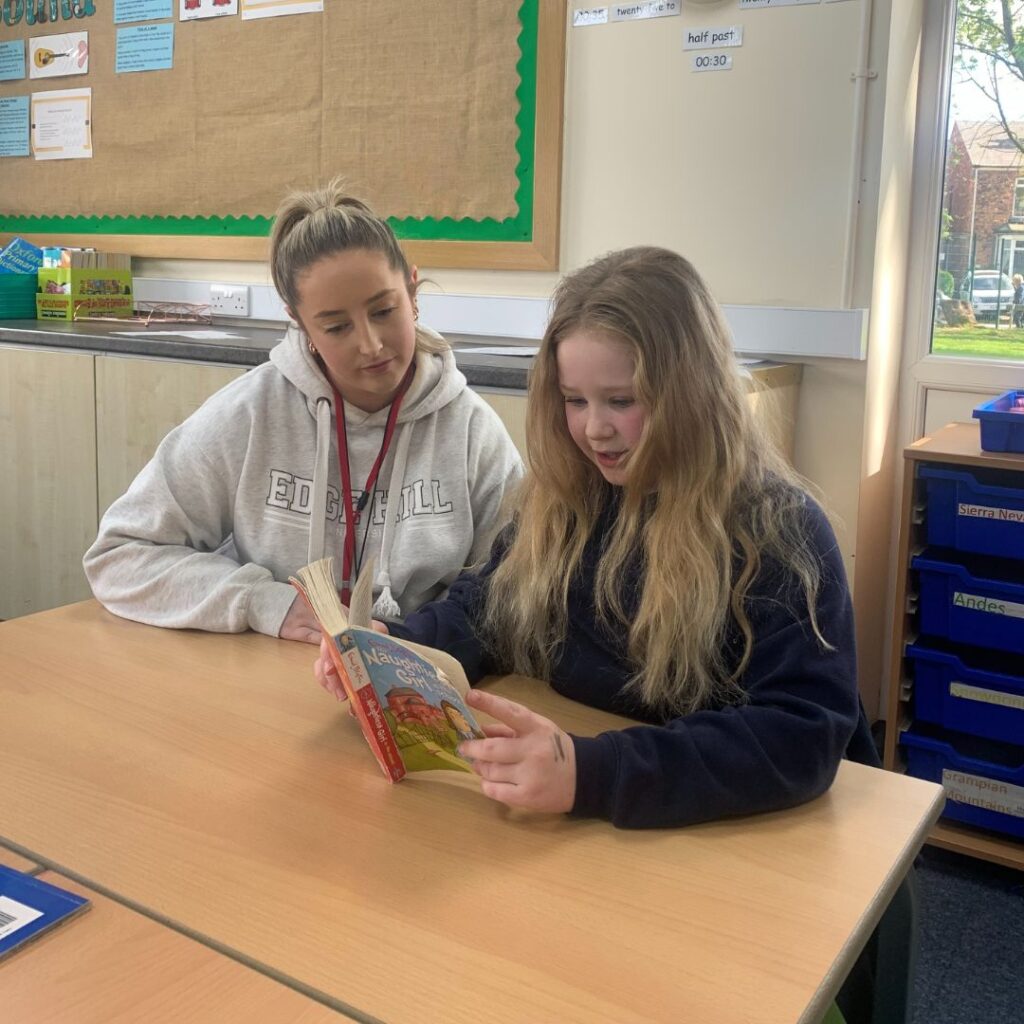student Erin McKenna reading a book with school pupil in classroom setting