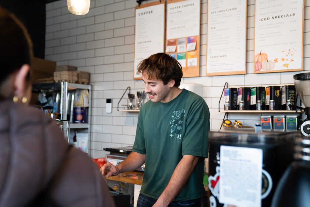 Barista serving students in local coffee shop in town centre