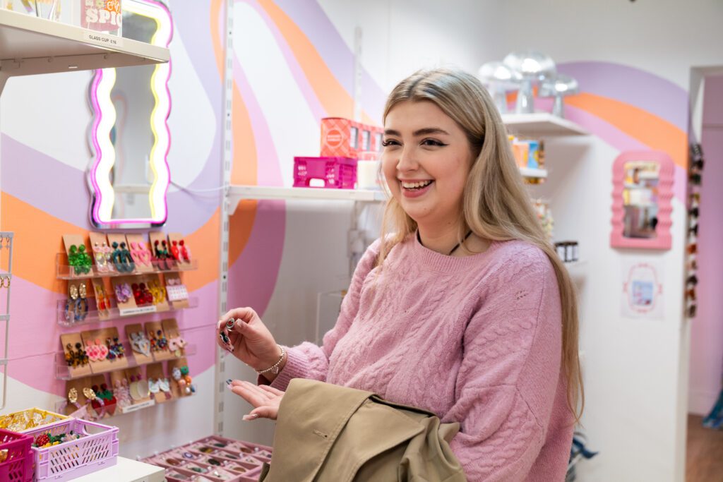 Student smilling next to display of jewellery in local independent store