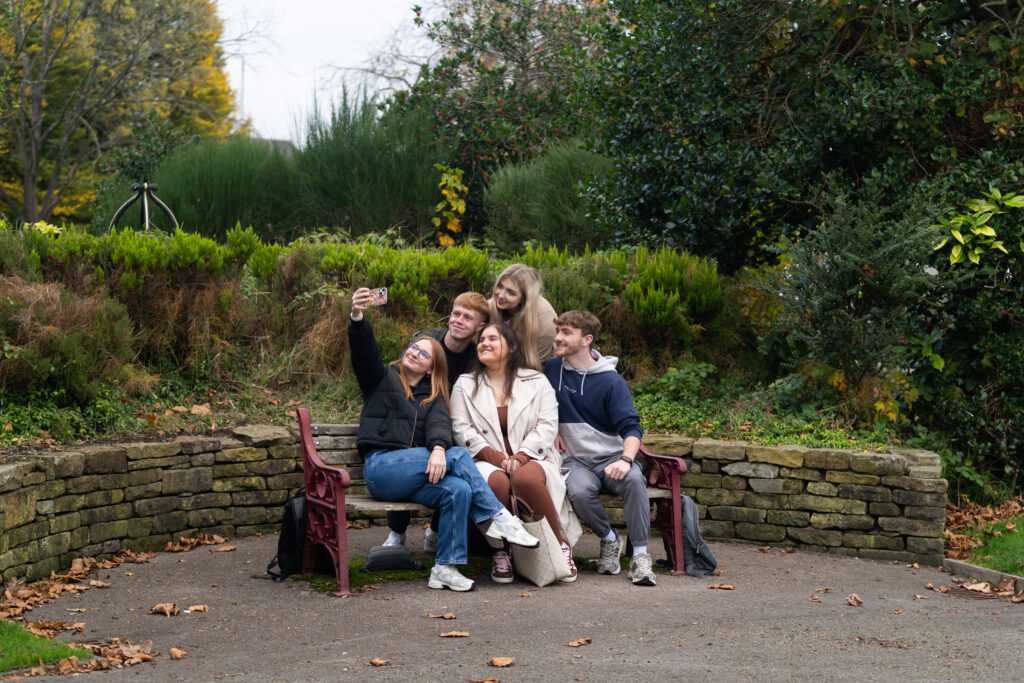 Students taking selfie togethe on bench in local park in Ormskirk