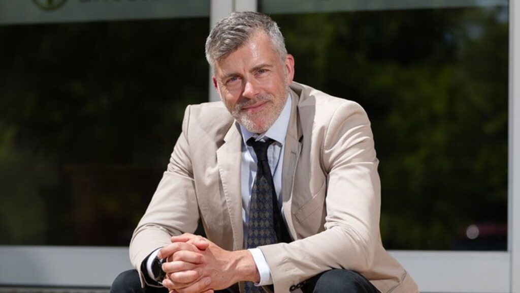 Professor Kurt Allman sits on steps, leans his arms on his knees and smiles the camera.